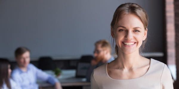 Female company director smiling with office colleagues in background.