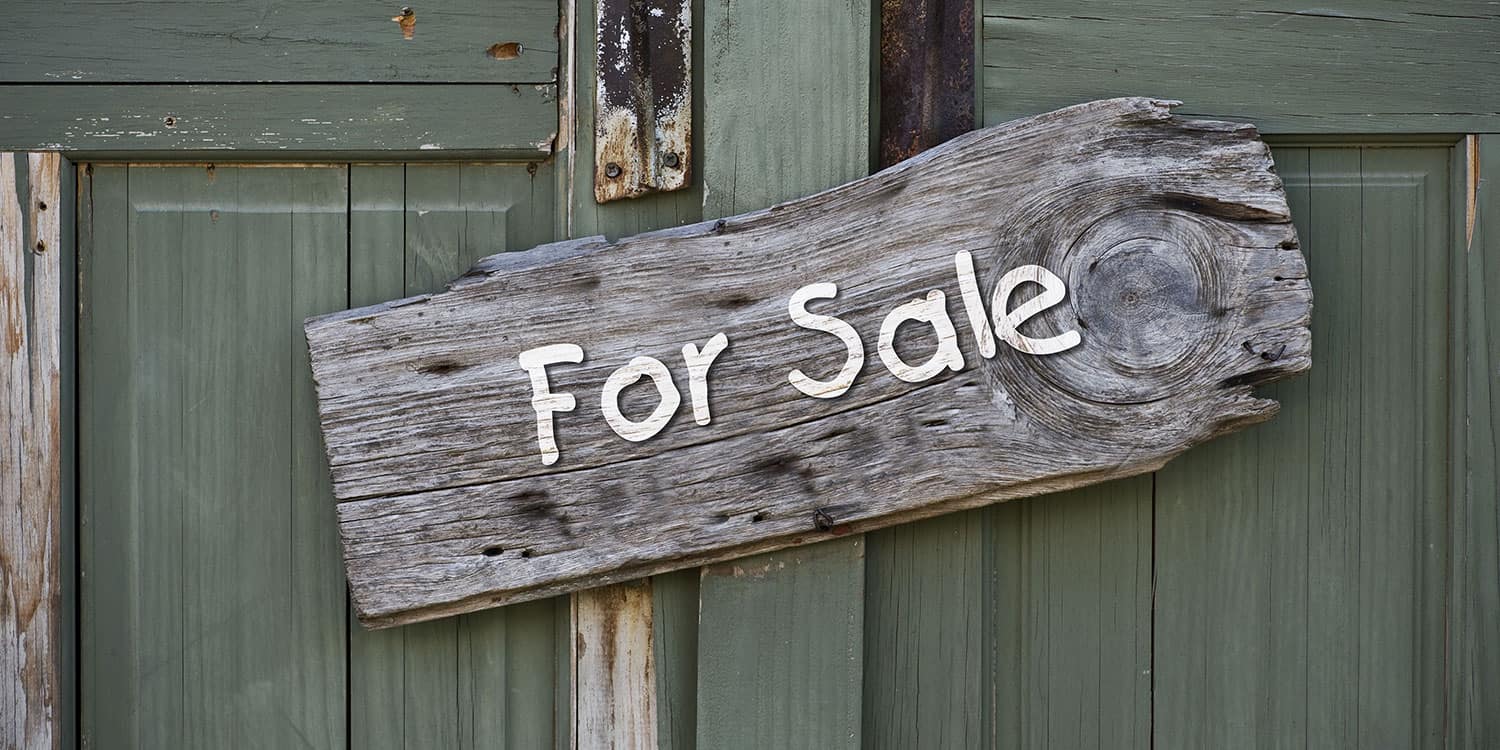 A wooden 'for sale' sign attached to a green door.