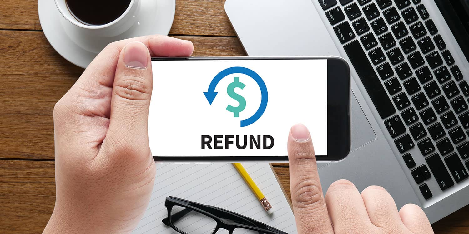 Image of a person holding a mobile phone with the screen displaying the dollar sign and the word 'REFUND'.