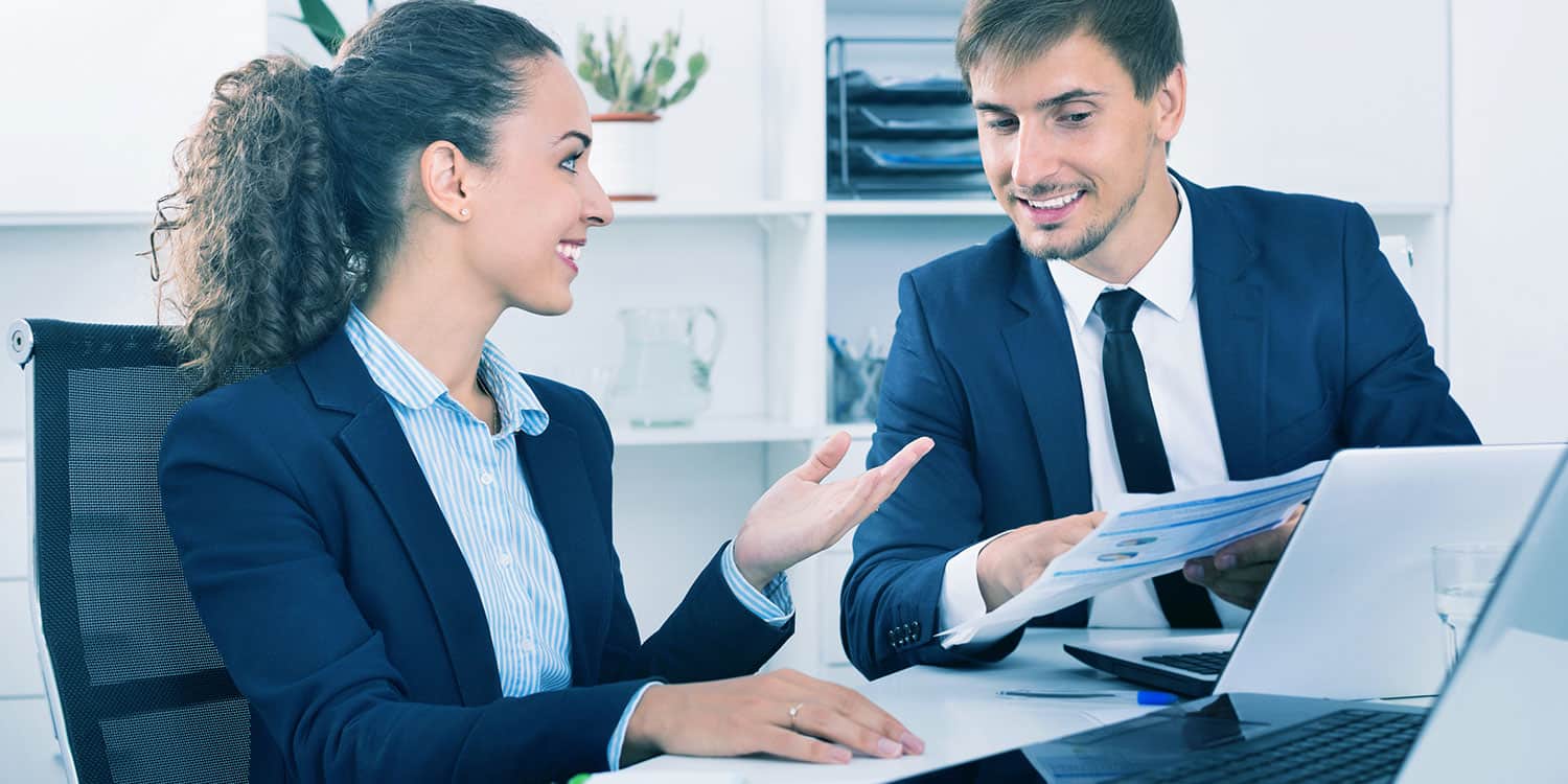 Two business people sitting at a desk whilst reviewing documents.