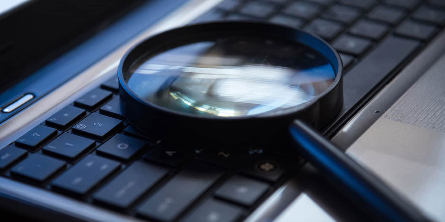 Magnifying glass lying on a black keyboard, illustrating that company details can be found online, including the registered office address.