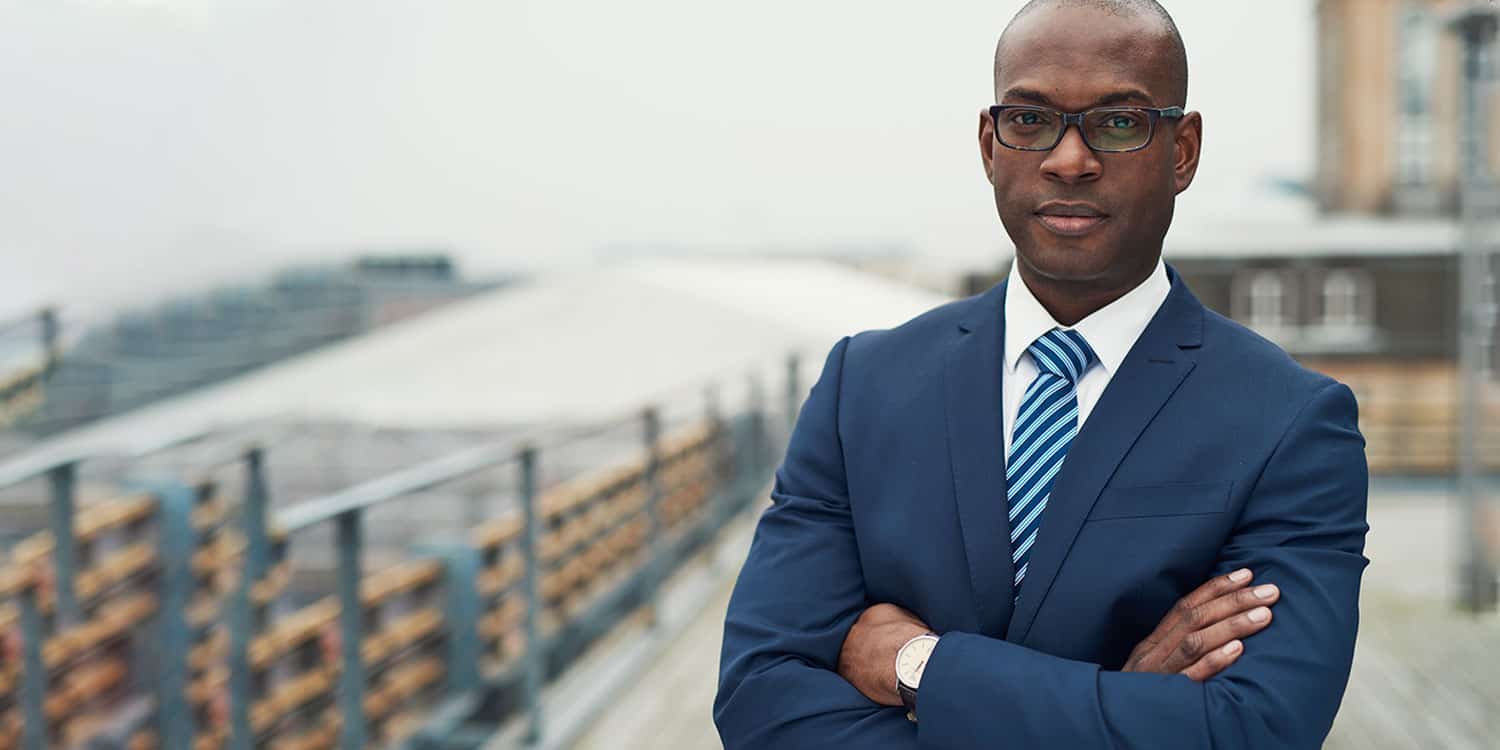 Company director in blue suit and tie crossing arms and smiling.