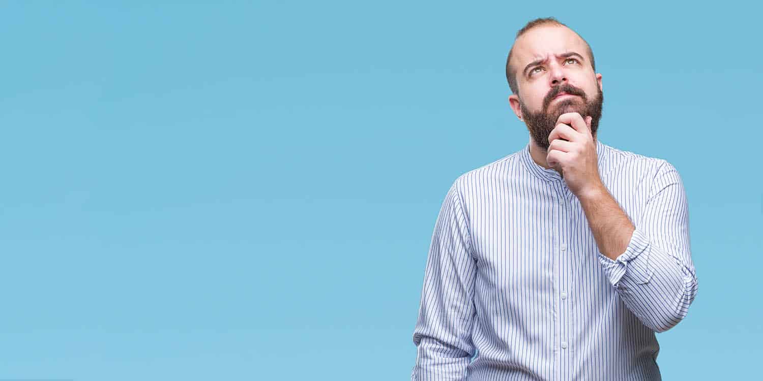 Image of a man with beard and light blue shirt holding his chin and looking upwards in contemplation.