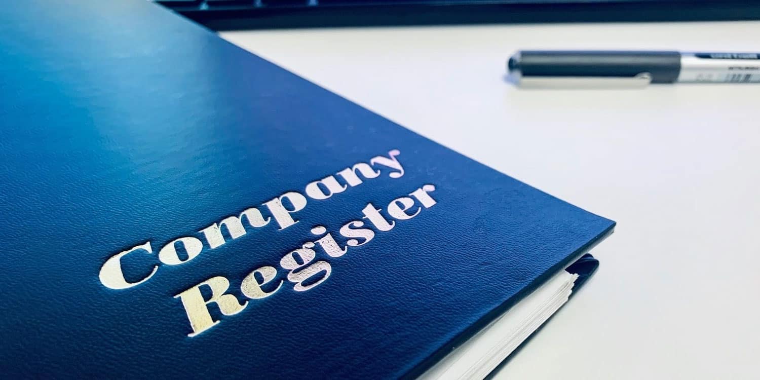 A navy blue ring binder folder titled Company Registers, lying on a desk.