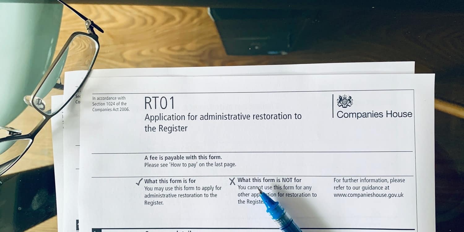 An RT01 form - Application for administrative restoration by the Registrar sitting on a glass desktop with spectacles and pen.
