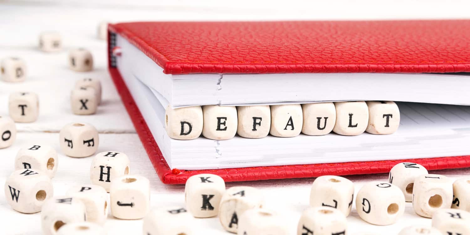 The word 'default' spelled out on a row of wooden blocks, set within the edge of a folded red notebook, illustrating that Model articles of association is the default set provided by Companies House.