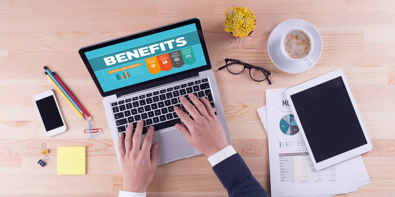 Business person working at a desk with laptop screen displaying the headline 'BENEFITS'.