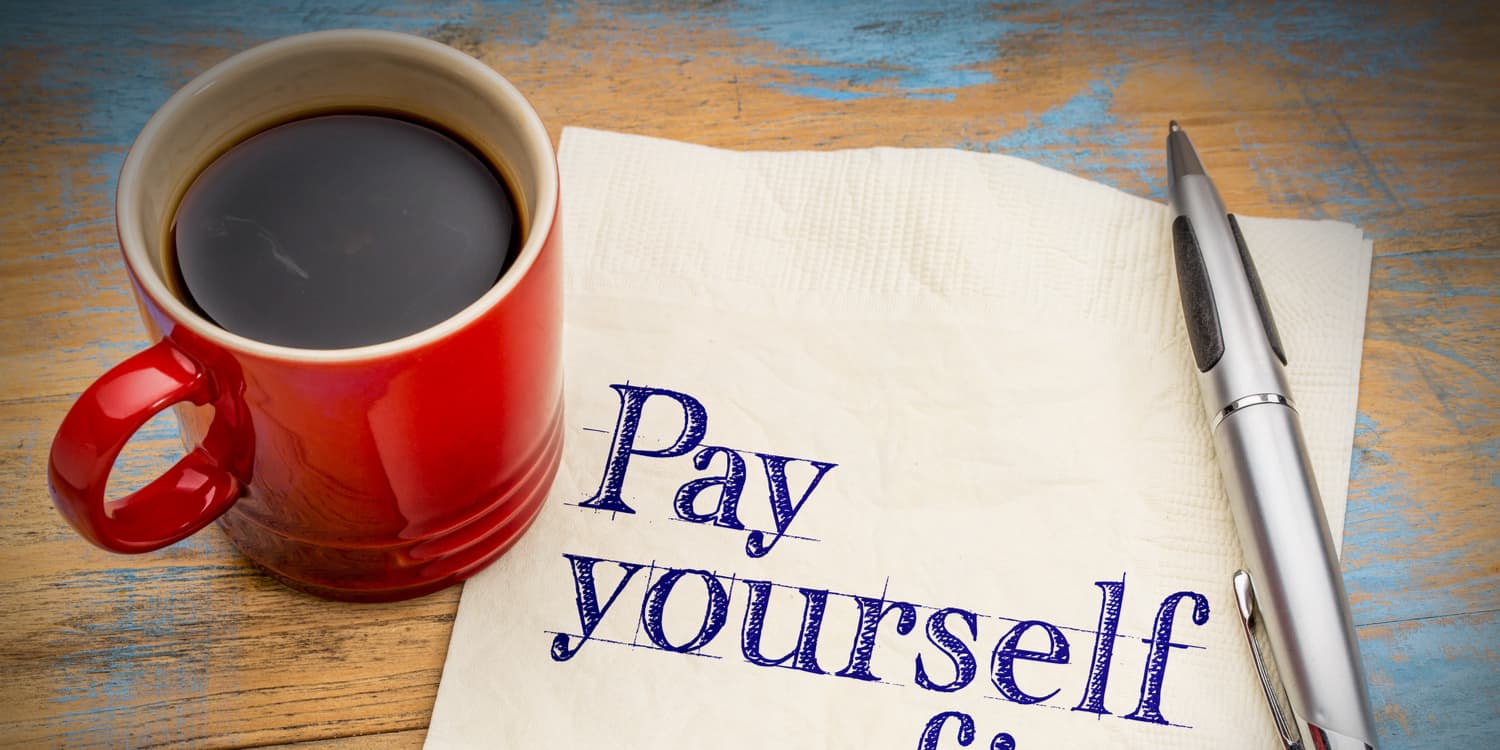 'Pay yourself' written on a napkin, with cup of coffee and pen also sitting on the table.