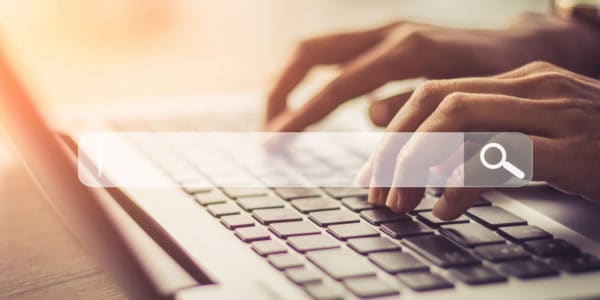 Hands typing on laptop keyboard with search bar overlaid centrally - soft focus picture.