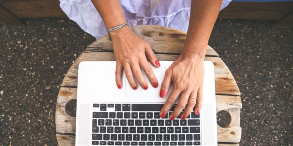 Woman typing on a laptop outdoors at a round wooden table, possibly researching or registering a company name for a new business venture