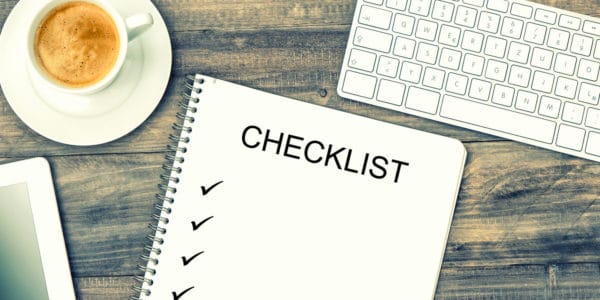 Notebook displaying the headline 'Checklist' with ticks, digital tablet pc, keyboard and coffee on wooden background.