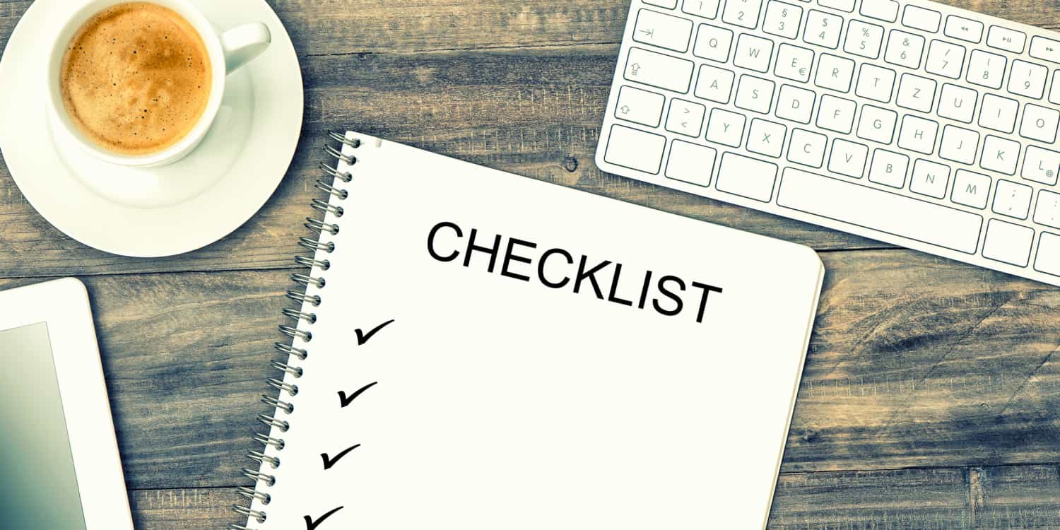 Notebook displaying the headline 'Checklist' with ticks, digital tablet pc, keyboard and coffee on wooden background.