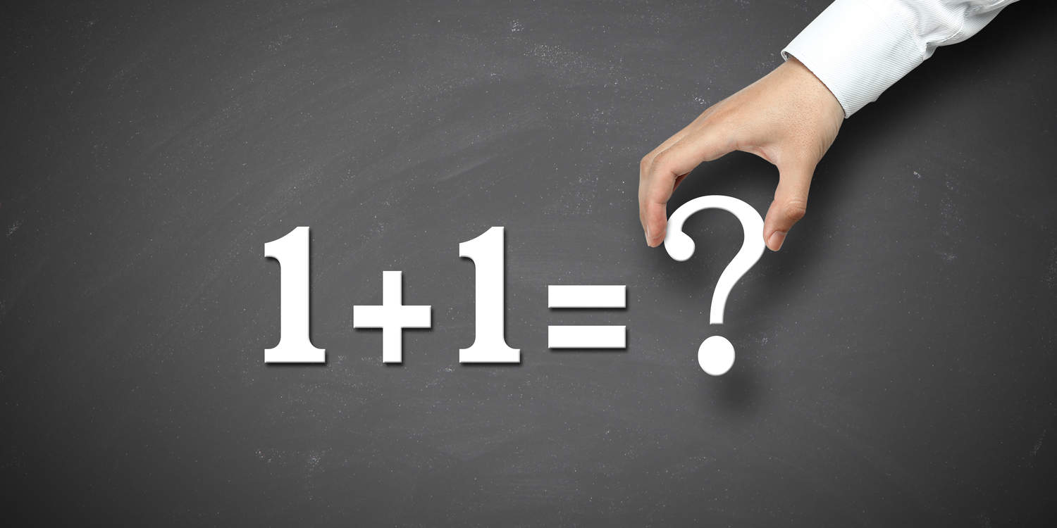 White magnetic numbers and symbols being placed on a blackboard displaying '1 + 1 = ?' illustrating the concept of whether 2 businesses can run under one company.