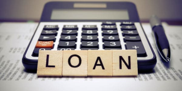 Wooden letter blocks spelling the word 'LOAN' with desktop calculator and pen in the background.