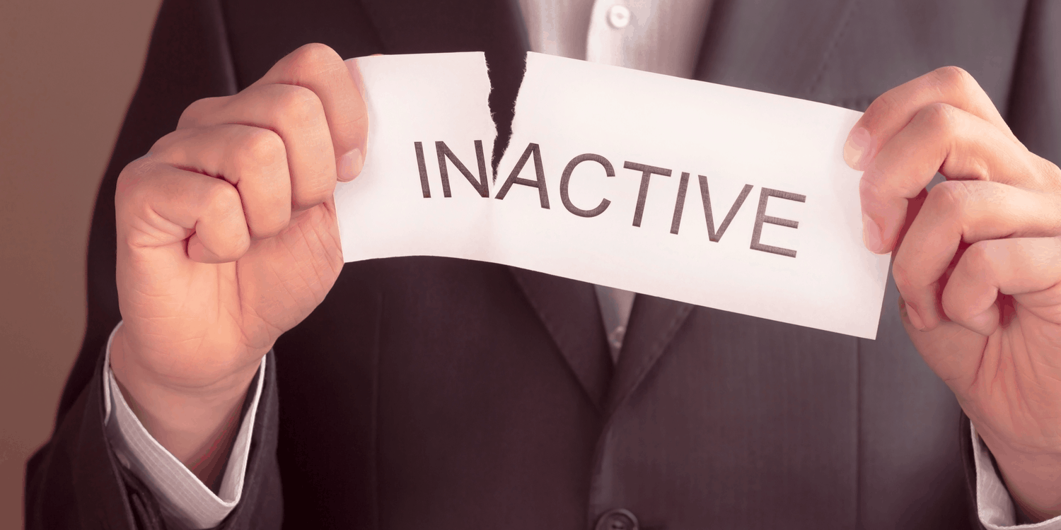 Businessman in dark grey suit tearing a piece of paper with the word INACTIVE printed on it in black font.