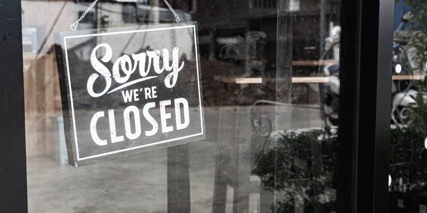 Black and white image of 'Sorry we're Closed' sign hanging in a shop window.