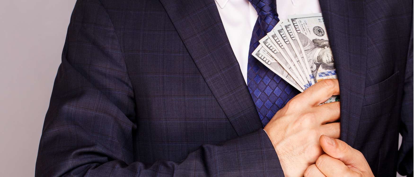 Businessman putting money in suit jacket pocket.