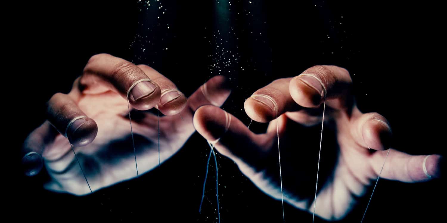 The hands of a puppet master controlling the strings of a puppet.