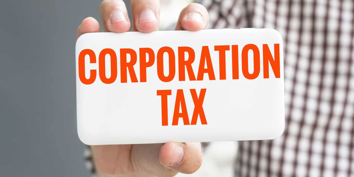 Man's hand haolding a white card with the phrase CORPORATION TAX in orange captial letters.