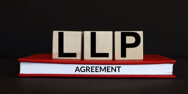 LLP AGREEMENT displayed on wooden cubes and red book, with black background.