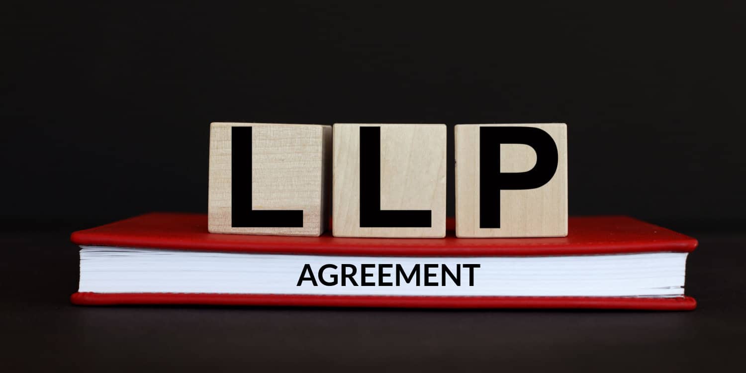 LLP AGREEMENT displayed on wooden cubes and red book, with black background.