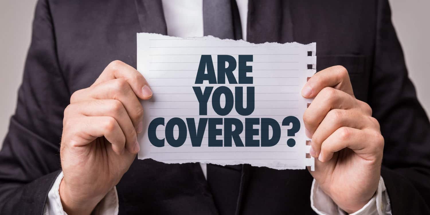 A businessman holding a sheet of paper with the words ARE YOU COVERED? printed in black capital letters. Illustrating the concept of the importance of business insurance.