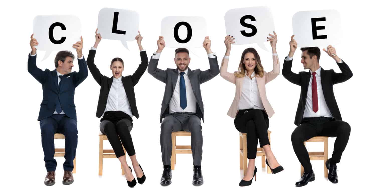 Five happy members of a close company sitting in a row and each holding up a white card with a letter spelling the word 'CLOSE'.