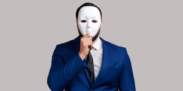 Portrait of a company shareholder wearing a blue suit with white shirt and tie, covering his face with a white mask, hiding his identity.