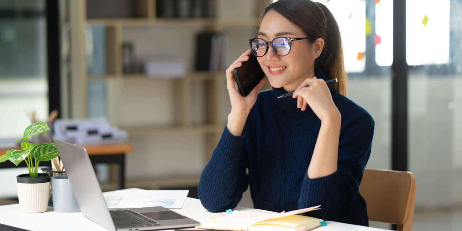 Smiling young businesswoman sitting at a desk with laptop and mobile phone - running her business from home.