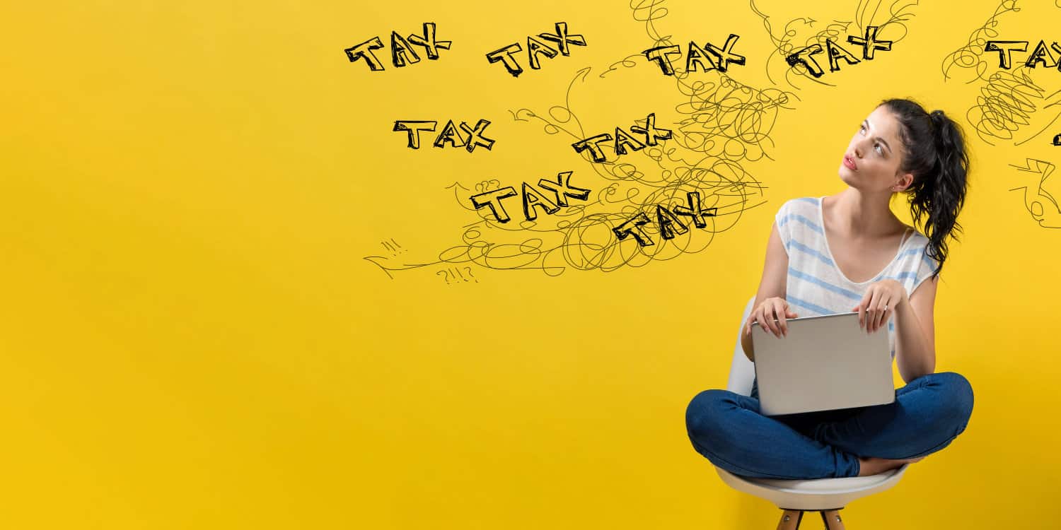 Young female business owner sitting on stool woith laptop and pondering her Company Tax Return.