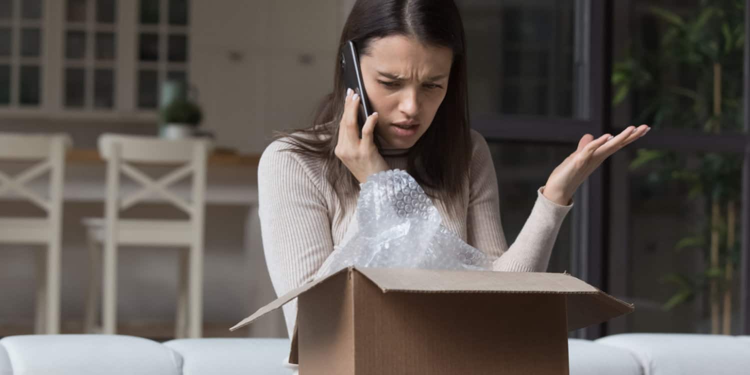 Dissatisfied customer, sitting on a sofa with opened cardboard box on her lap and making a phone call to make a customer complaint.