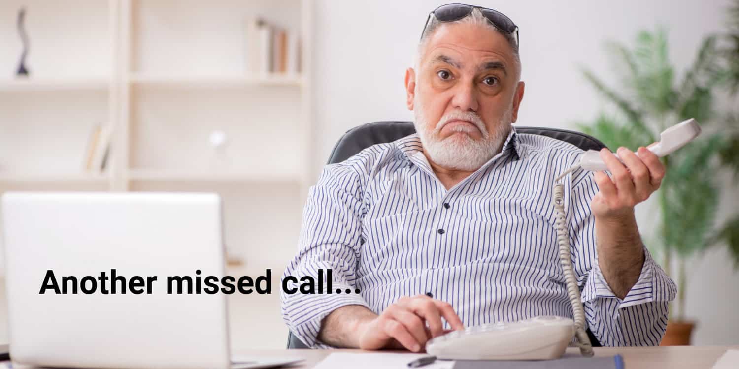 Mature businessman sitting at his desk and holding telephone receiver, with a resigned look on his face after another missed call.