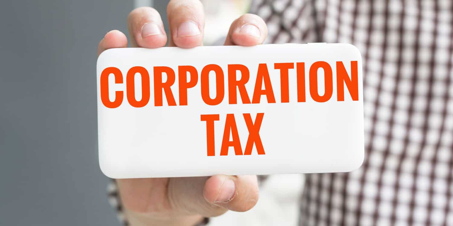 A man's hand holding up a white card with the words CORPORATION TAX displayed in orange text.