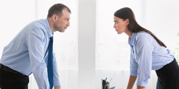 A businessman and businesswoman, representing an accountant and a bookkeeper staring at each other over a desk.