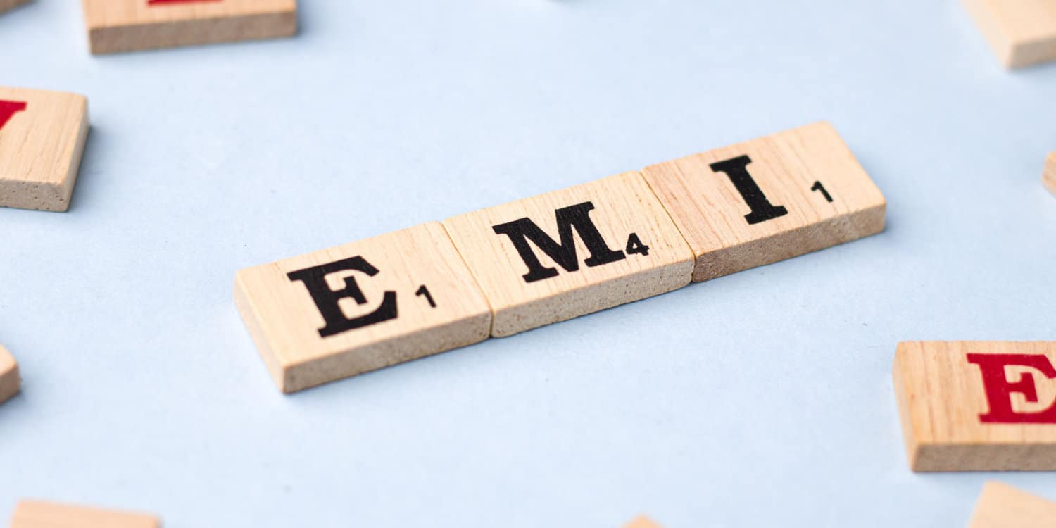 Three scrabble tiles spelling 'EMI' with other scrabble tiles randomly scattered on a light blue desktop.