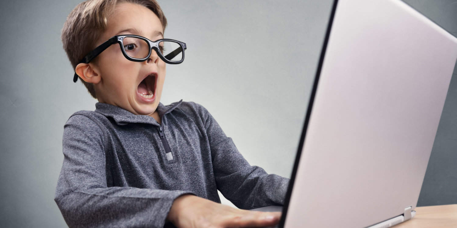 Young businessman, with large black rimmed spectacles, sitting at a desk and working on his laptop, aghast at finding a mistake in his Self Assessment tax return.