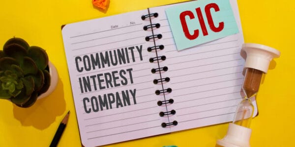 Open notebook lying on a yellow desk with COMMUNITY INTEREST COMPANY and CIC displayed on the pages.