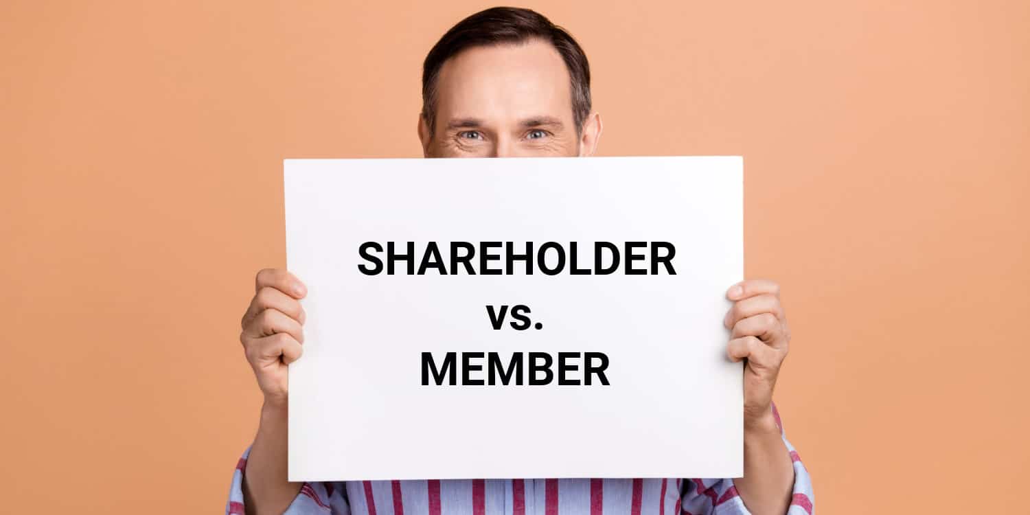 Buisnessman holding up a large white card with the headline SHAREHOLDERS vs MEMBERS displayed in large black text.