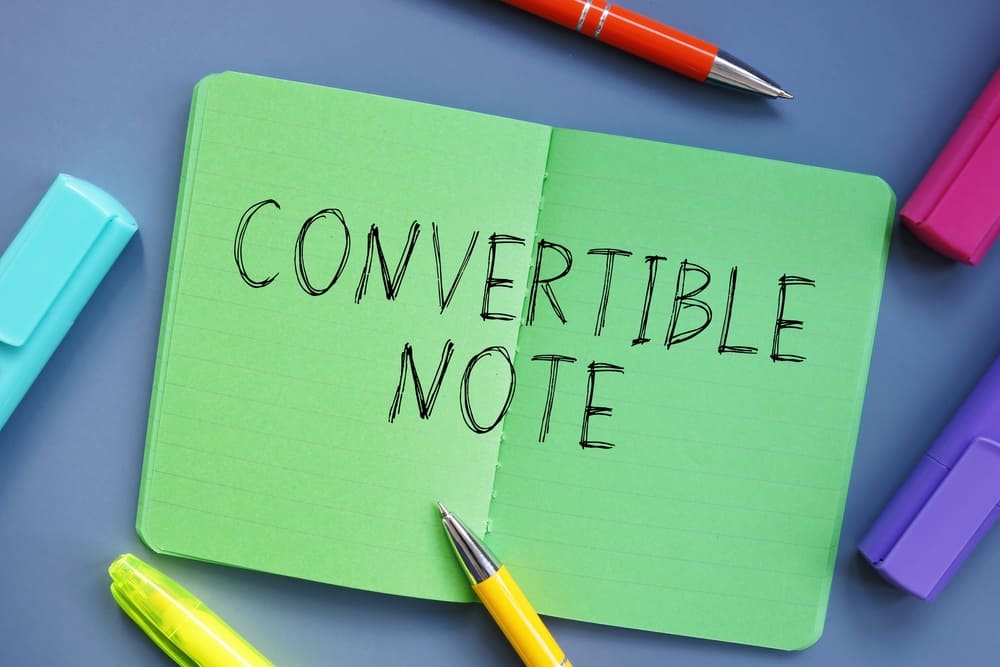 Green note pad lying on a desk with 'CONVERTIBLE NOTE' written in large capital letters.