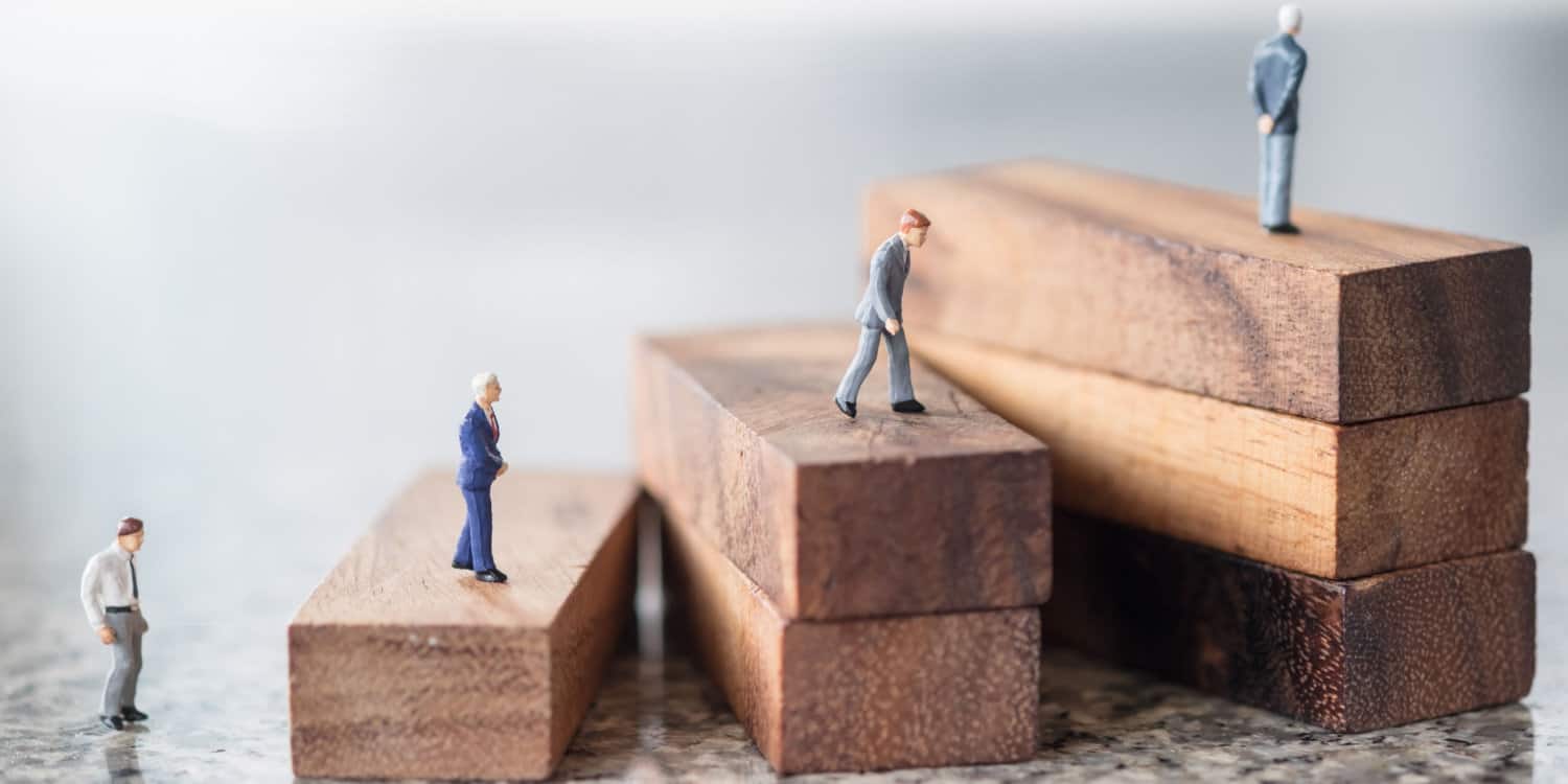 Miniature businessmen figures walking and standing on wood stair made from wooden blocks, illustrating the succession concept.