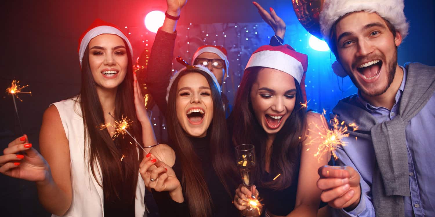Group of beautiful young office workers celebrating in Santa hats and throwing colourful confetti at the office Christmas party.