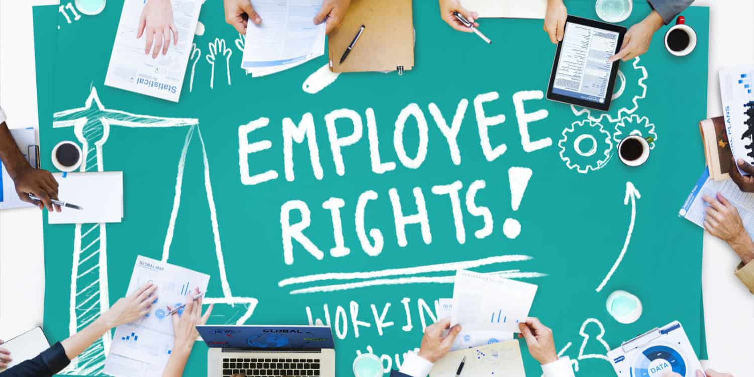 Overhead view of people working at a green table with the words 'EMPLOYEE RIGHTS!' displayed on the table surface. Employment Law concept image.
