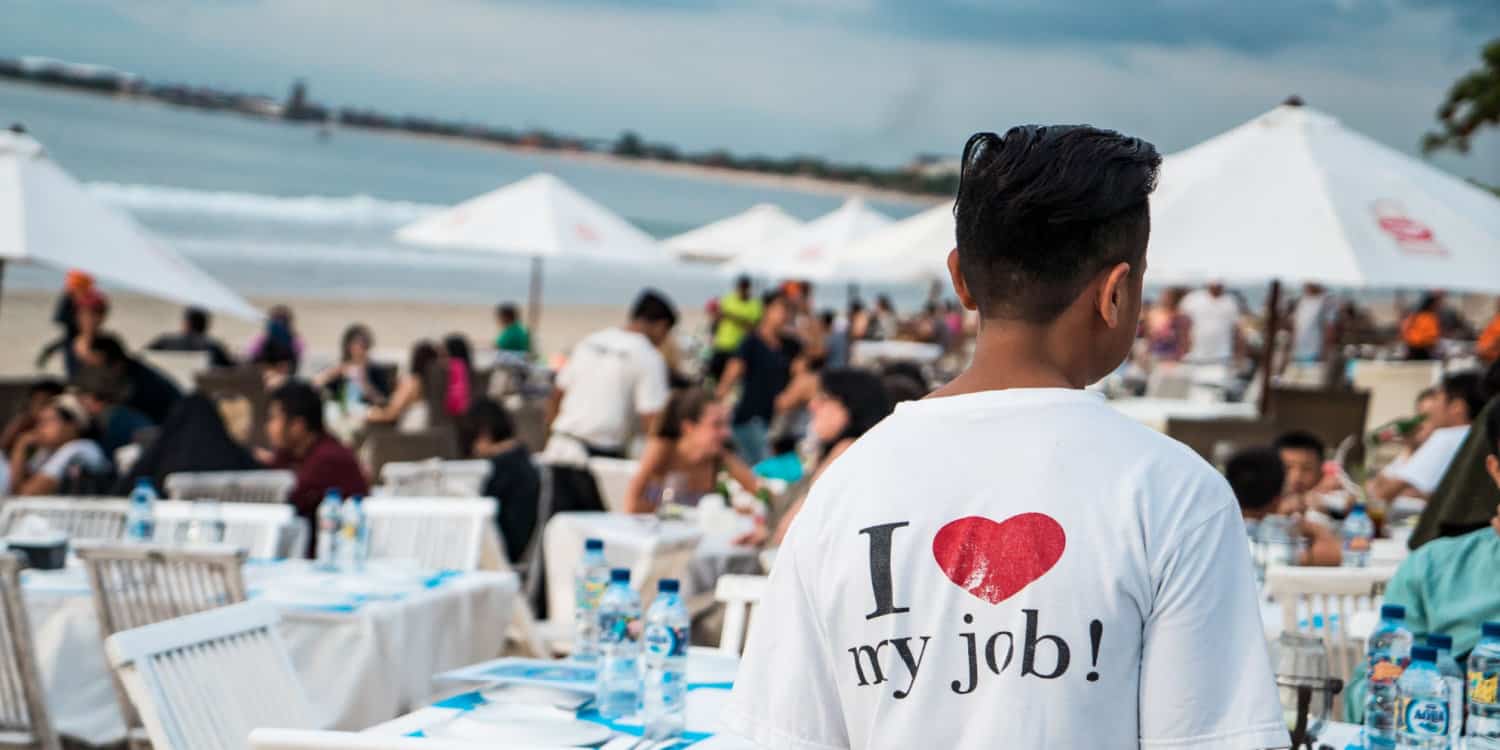 A young man wearing a T-shirt "I love my job" while working at a holiday beach club.