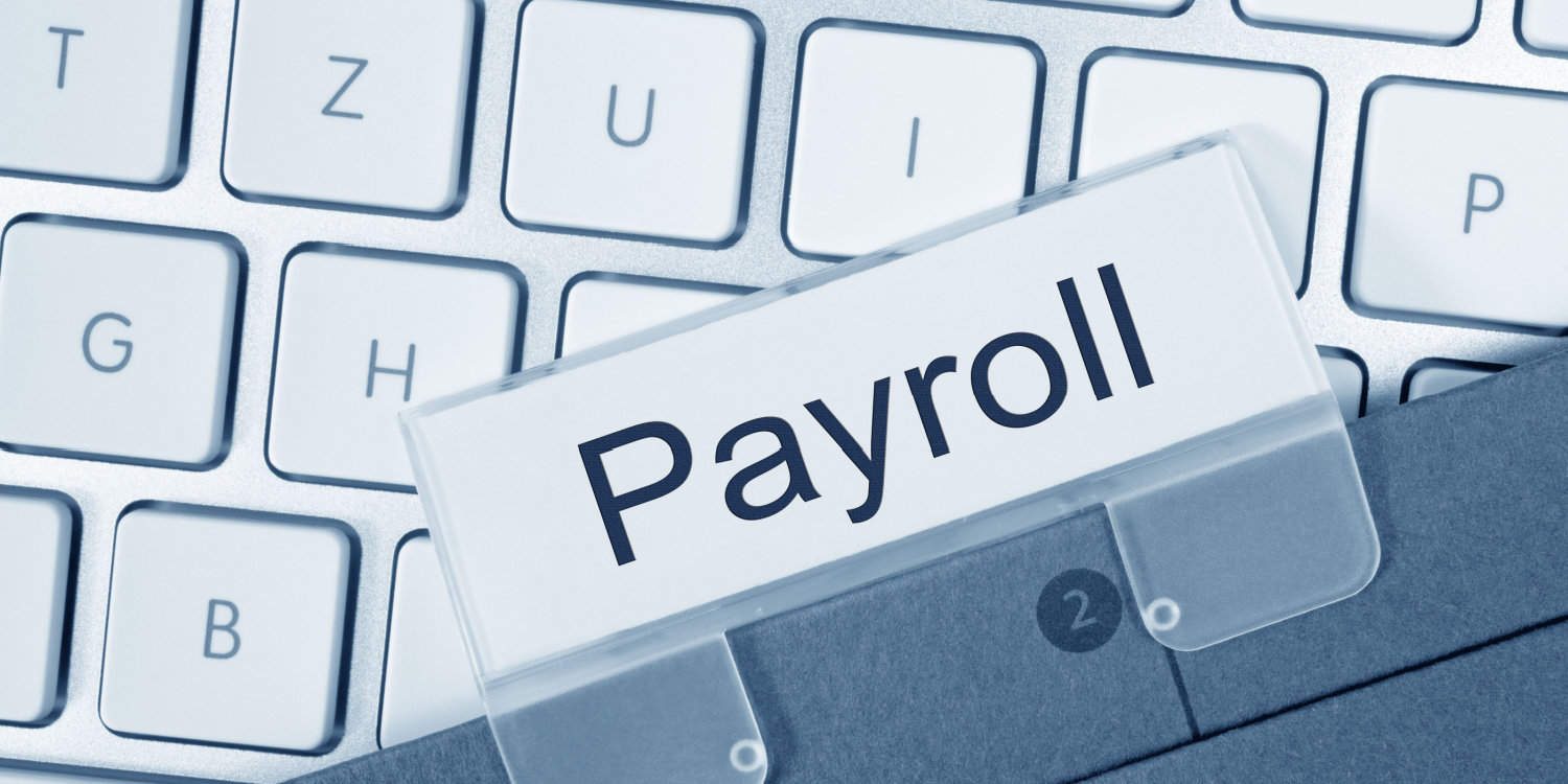 Close up shot of a cardboard file labelled 'Payroll' lying on a laptop keyboard.