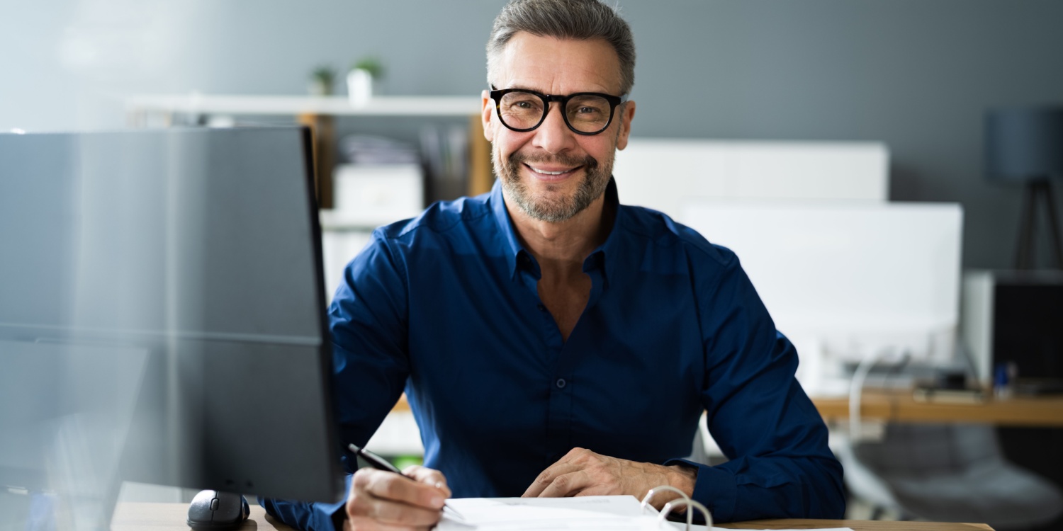 Accountant sitting at his desk wearing a blue shirt, working on his company's statutory reporting.