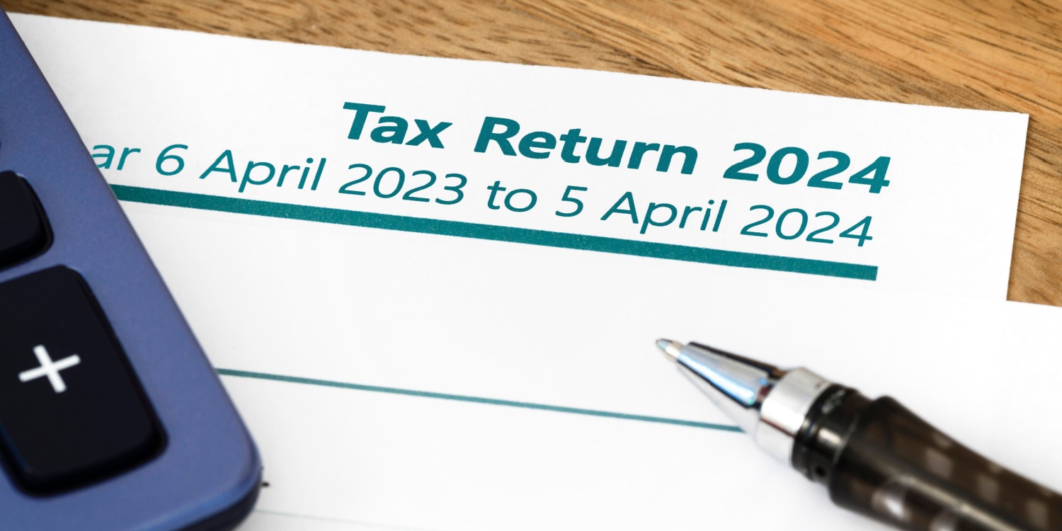 UK Self Assessment tax return form for 2023-24, lying on a wooden desk with a calculator and pen.