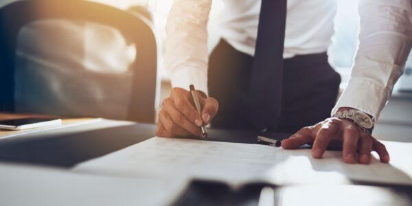 A business professional in formal attire signs paperwork at a desk, with a smartphone and documents nearby, during the formal process of members' voluntary liquidation.