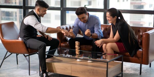 Three coworkers playing Jenga in an office, symbolising strategic risk in business.