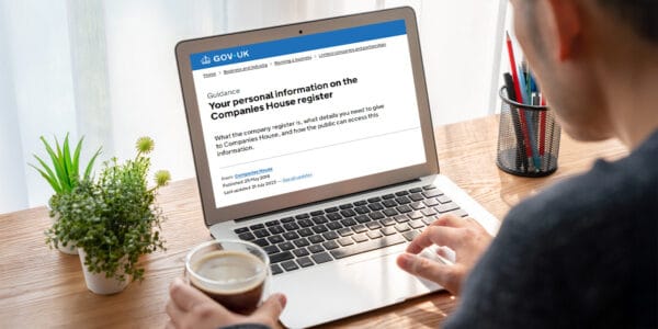 Person reviewing Companies House updates on a laptop, specifically guidance about personal information on the register, with a coffee cup in hand