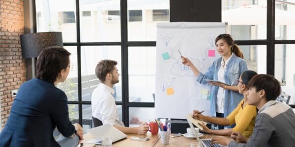 A young woman demonstrates leadership as she presents ideas on a flipchart to her team during a meeting in a modern office setting